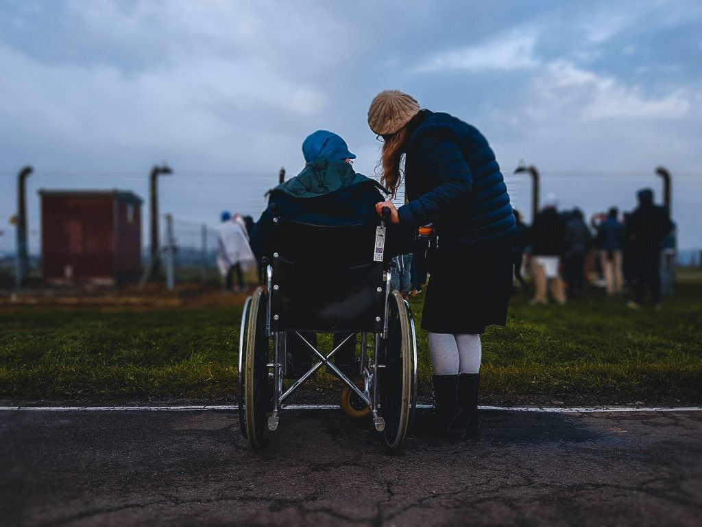 photo from the back of one person in a wheelchair and another standing next to them