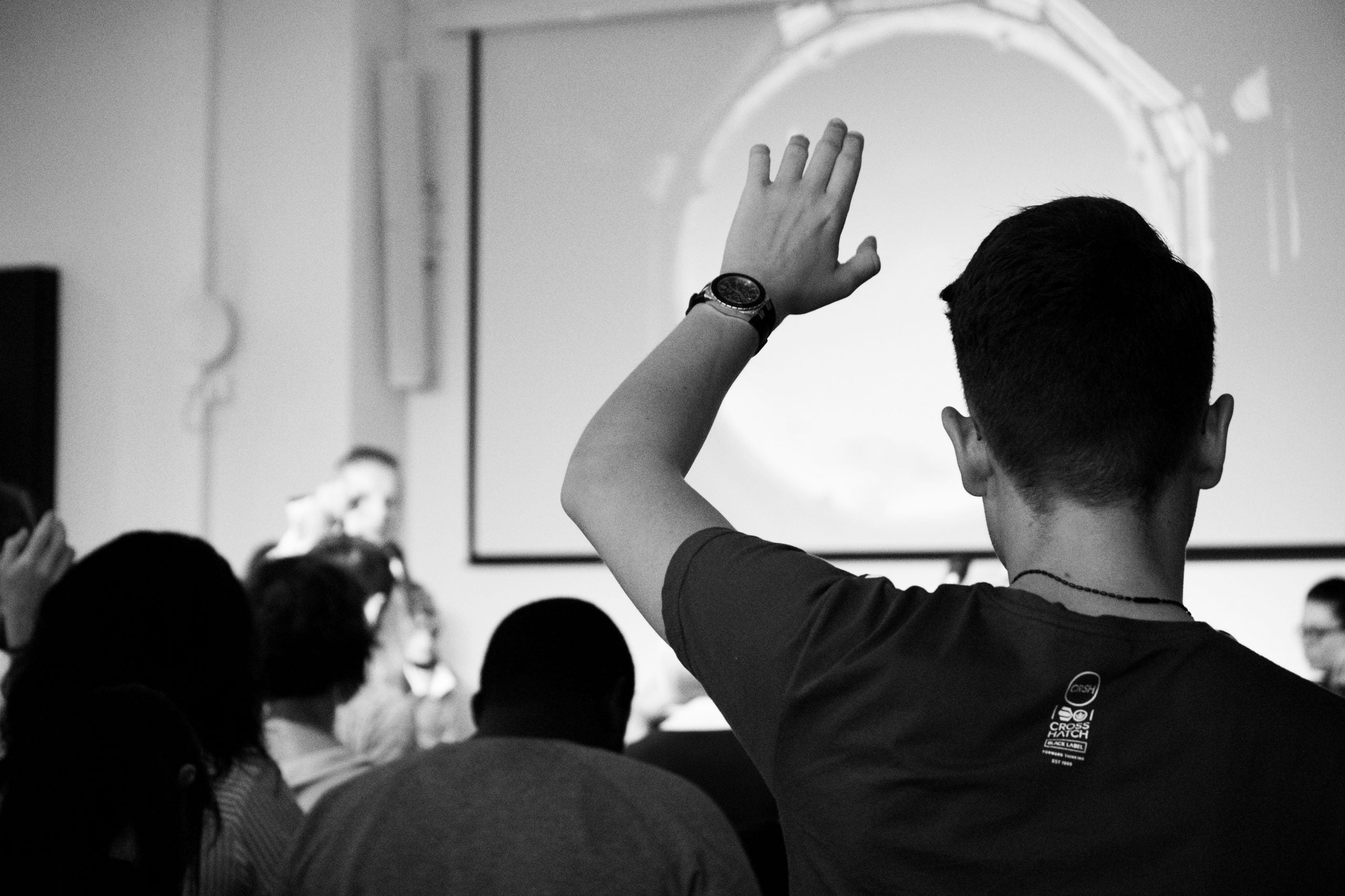 back of a person's head as they raise their hand from the audience during an event