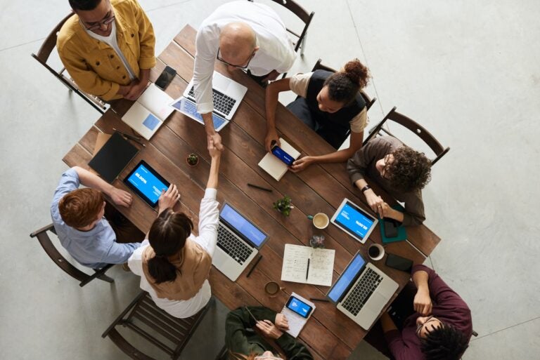 overhead shot of a meeting table, with 8 diverse people discussing and shaking hands