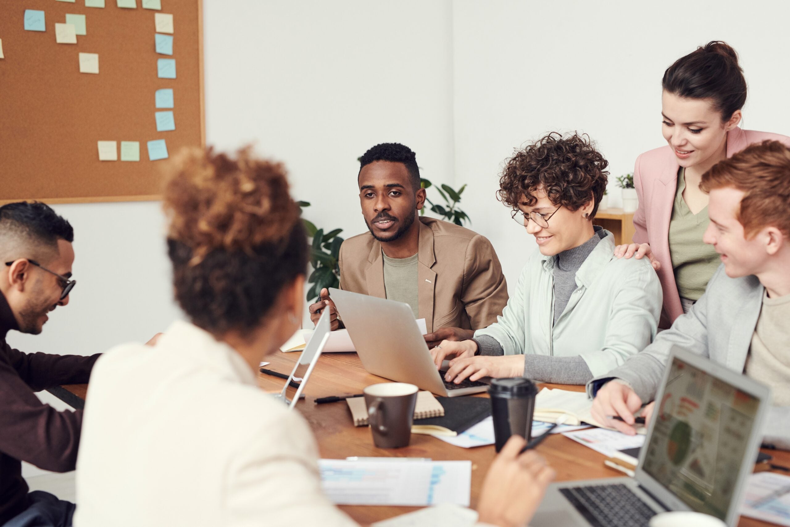 a large, diverse group of coworkers meeting and discussing something over a shared table with papers and laptops