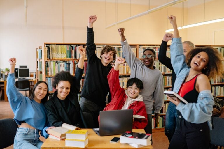 diverse group of 7 students in a library space cheering