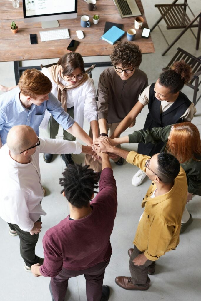 diverse group of colleagues putting their hands together in solidarity in an office space