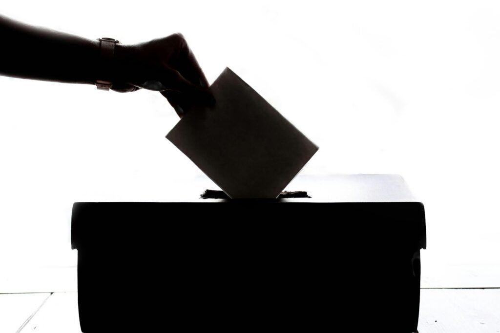 silhouetted image of a hand dropping off a ballot in a voting box